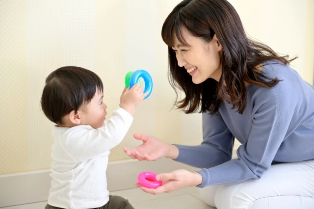 輪のおもちゃを手渡して親子で遊ぶ様子のイメージ写真